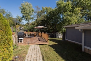 Ein Garten mit einer Holzterrasse, Grill und einer überdachten Patio.