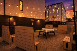 An outdoor seating area with wooden benches and a table, string lights, and a brick floor. - 8 Beds Near Broadway | Each Room Has Own Bath (Nashville)