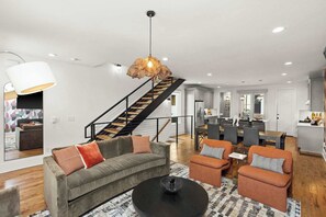 Een moderne woonkamer met een bank, fauteuils en een salontafel. Een trap leidt naar de bovenverdieping.