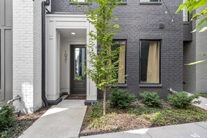 A modern two-story house with a dark brick exterior, a white front door, and a small tree in the front yard. - Bourbon & Ballads: Karaoke Stage, Sauna + Rooftop (Nashville)