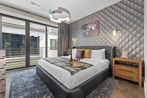 A modern bedroom with a large bed, a nightstand, a wall-mounted TV, and a balcony with a view. - Bourbon & Ballads: Karaoke Stage, Sauna + Rooftop (Nashville)