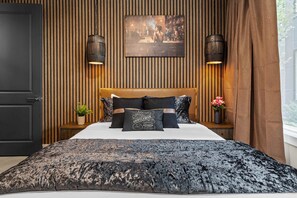Una camera da letto con un letto, parete rivestita in legno, due lampade a parete, un quadro e una finestra con tende.