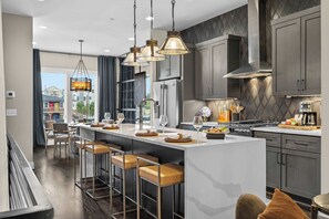 A modern kitchen with a central island, bar stools, stainless steel appliances, and pendant lighting. - Bourbon & Ballads: Karaoke Stage, Sauna + Rooftop (Nashville)