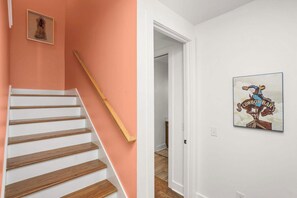 Een trap met houten treden en een leuning, die leidt naar een kamer met een witte muur en een ingelijst kunstwerk.