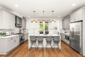 A modern kitchen with white cabinets, a central island with bar stools, stainless steel appliances, and pendant lighting. - Prime Spot Minutes to 12 South, Gulch & Broadway (Nashville)