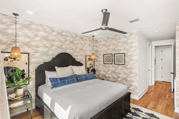 Un dormitorio con cama, ventilador de techo, lámparas de noche y una planta.