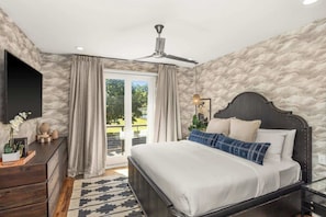 Un dormitorio con cama, ventilador de techo, cómoda y ventana con cortinas.