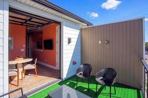 Een klein terras buiten, met een tafel en stoelen, een houten hek en een deur die naar een binnenruimte leidt.