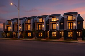 Una hilera de casas adosadas modernas de varios pisos, con ventanas amplias y balcones, al atardecer.
