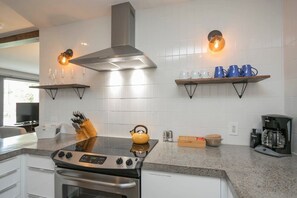 A modern kitchen with a built-in stove, oven, and a stainless steel range hood. There are two wall-mounted shelves with cups and glasses, and a coffee maker on the counter. - Yard, Parking, 4.5 Mi to Bway (Nashville)