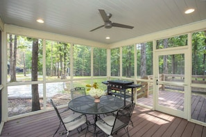 A covered patio with a round table and chairs, a grill, and a ceiling fan. - Bobwhite at Buckhorn Hollow (McEwen)