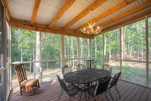 A covered outdoor area with a round table and chairs, large windows, and a wooden ceiling. - The Roost at Buckhorn Hollow (McEwen)