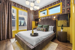 A bedroom with a large bed, a bedside table, a mirror, and a window with curtains. - City Views | Rooftop Deck | Fire Pit + Grill (Nashville)