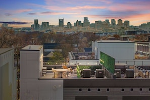 Eine Dachterrasse mit Sitzgelegenheiten im Freien, Klimaanlagen und Blick auf eine städtische Skyline bei Sonnenuntergang.
