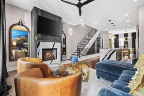 Ein modernes Wohnzimmer mit Ledersofas, einem Kamin, einem großen Fernseher und einer Treppe, die zu einer weiteren Ebene führt.