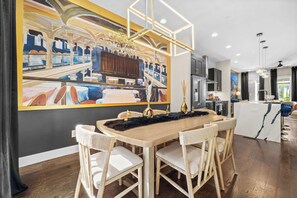 A modern dining area with a wooden table, wicker chairs, and a large painting on the wall. - Karaoke Murals Rooftop Parking Near Broadway (Nashville)
