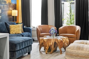 A living room with a blue sofa, two brown leather chairs, a wooden coffee table, and a view of a brick building through large windows. - Karaoke Murals Rooftop Parking Near Broadway (Nashville)