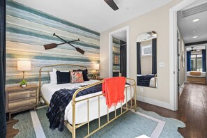 A bedroom with a bed, nightstands, a wall mural, a mirror, and a view into another room. - Karaoke Murals Rooftop Parking Near Broadway (Nashville)