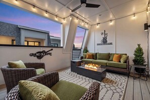 A rooftop terrace with wicker furniture, a fire pit, string lights, and a view of the sunset. - Elegant Nash Karaoke Haven w/ Rooftop Fire Table (Nashville)