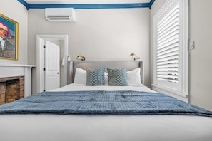 A bedroom with a bed, two bedside lamps, a door, and a window with blinds. - The Madison Suite | Germantown Inn | Breakfast (Nashville)