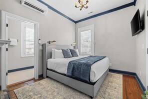 A bedroom with a bed, two bedside tables, a flat-screen TV, and a chandelier.