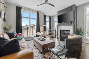 A modern living room with a leather sofa, a tufted armchair, a wooden coffee table, and a fireplace. - Gated Luxury | Broadway Views | Rooftop Fire Pit (Nashville)