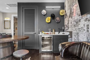 A modern kitchen with a built-in oven, a dining area with a wooden table and a leather couch, and a wall decorated with hats and newspaper clippings. - Gated Luxury | Broadway Views | Rooftop Fire Pit (Nashville)