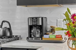 A modern kitchen with a coffee maker, a kettle, and a box labeled "STASH". - Gated Luxury | Broadway Views | Rooftop Fire Pit (Nashville)