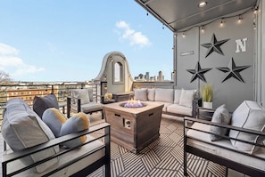 A rooftop terrace with a fire pit, seating area, and decorative stars on the wall. - Gated Luxury | Broadway Views | Rooftop Fire Pit (Nashville)