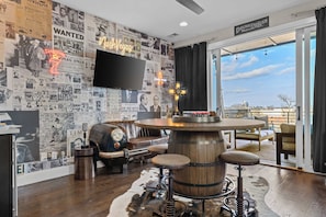 A bar area with a vintage theme, featuring a round wooden bar, stools, and a neon sign. - Gated Luxury | Broadway Views | Rooftop Fire Pit (Nashville)