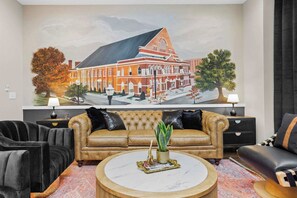 A living room with a large painting of a building, a brown leather sofa, a round coffee table, and black and brown armchairs. - Luxury Gated Duo Sleeps 24 Karaoke & Rooftop (Nashville)