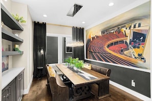 A dining area with a long wooden table, dark wooden chairs, a chandelier, and a large mural of an auditorium on the wall. - Luxury Gated Duo Sleeps 24 Karaoke & Rooftop (Nashville)