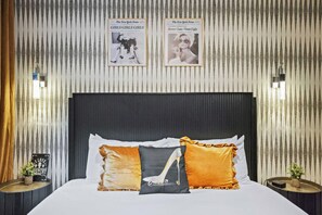 A hotel room with a bed, pillows, a headboard, two framed newspaper articles, and a small table with a plant. - Luxury Gated Duo Sleeps 24 Karaoke & Rooftop (Nashville)