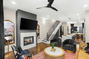 A modern living room with a fireplace, a flat-screen TV, a staircase, and a dining area. - Luxury Gated Duo Sleeps 24 Karaoke & Rooftop (Nashville)