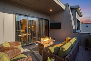An outdoor patio with wicker furniture, a fire feature, and a glass door leading to an indoor area. - Luxury Gated Duo Sleeps 24 Karaoke & Rooftop (Nashville)