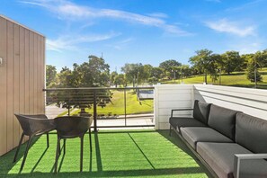A balcony with a green artificial turf floor, a black sofa, and two black chairs. - 8th Ave South Gem Fabulous Home for Groups of 12 (Nashville)