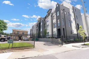 A modern multi-story building with a gated entrance, a parking area, and a sign indicating pet-friendly services. - Sleeps 24! Broadway Views, Rooftops & Karaoke (Nashville)