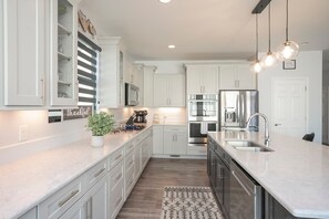 A modern kitchen with white cabinetry, stainless steel appliances, and pendant lighting. - New Hot Tub, Spacious, Near Downtown (Nashville)
