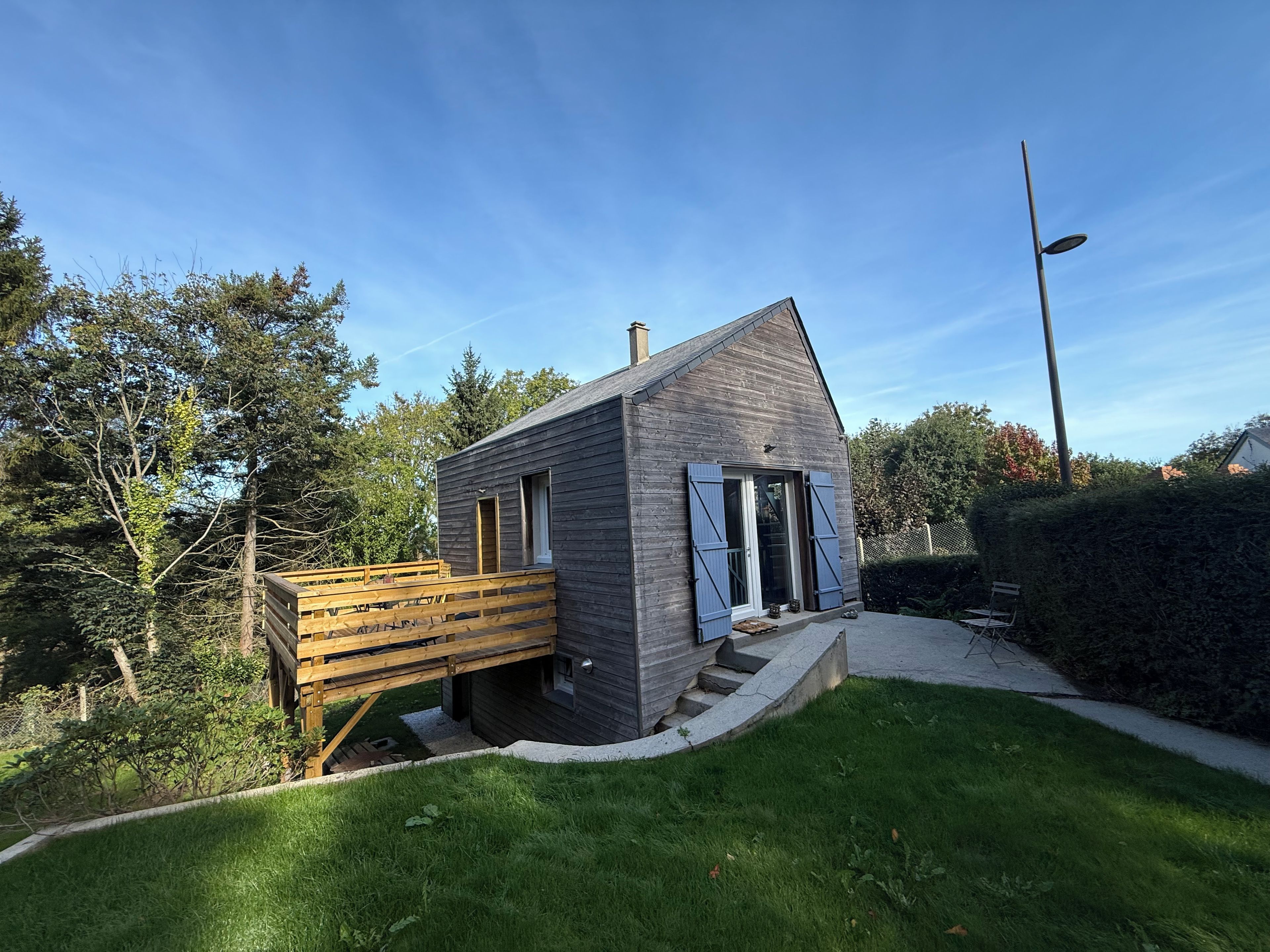 Ett litet, modernt hus med en träveranda och en stensatt gång som leder till entrén.