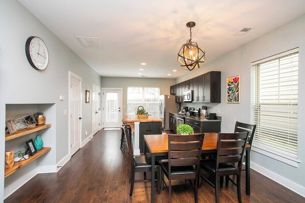 A modern kitchen with dark cabinetry, a central island, and a dining area with a wooden table and chairs. - Relaxing 2 BD/2.5 BA Nash Home (Nashville)