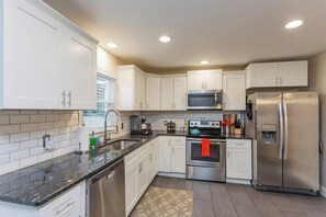 A modern kitchen with white cabinets, stainless steel appliances, and a black countertop. - East Nash Cottage 3 Miles to Downtown! (Nashville)