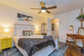 A bedroom with a bed, bedside tables, a desk, a ceiling fan, and a door leading to another room. - East Nash Cottage 3 Miles to Downtown! (Nashville)