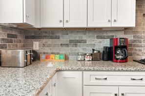 Eine Küche mit weißen Schränken, einer Granitarbeitsplatte, einem Toaster, einer Kaffeemaschine und Gewürzgläsern.