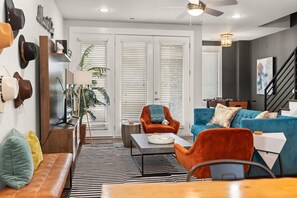 Ein modernes Wohnzimmer mit Sofa, Sessel und Couchtisch. Eine Treppe und eine Tür mit Jalousien sind ebenfalls vorhanden.
