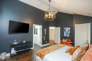 Une chambre moderne avec un grand lit, un téléviseur à écran plat, une console et une porte donnant sur une autre pièce.