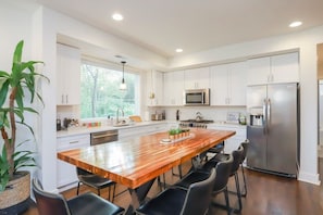 A modern kitchen with white cabinets, a wooden island, black chairs, and a stainless steel refrigerator. - Walk to 12 South & 8th Ave! 4BR/4BA (Nashville)