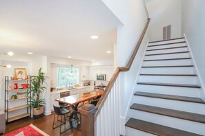 Une cuisine moderne dotée d’un îlot central, d’un escalier en bois et d’un coin repas avec des chaises.