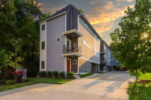 Un immeuble résidentiel moderne à deux étages, avec une façade grise, une porte rouge et un balcon au deuxième étage.