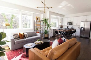 Un salon moderne avec un canapé gris, un divan en cuir marron et un coin repas comprenant une table et des chaises.