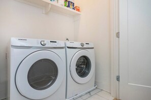Two Samsung front-loading washing machines in a laundry room with a white door and a shelf above. - 2 Side by Side Homes with Rooftops -Sleeps 24 (Nashville)